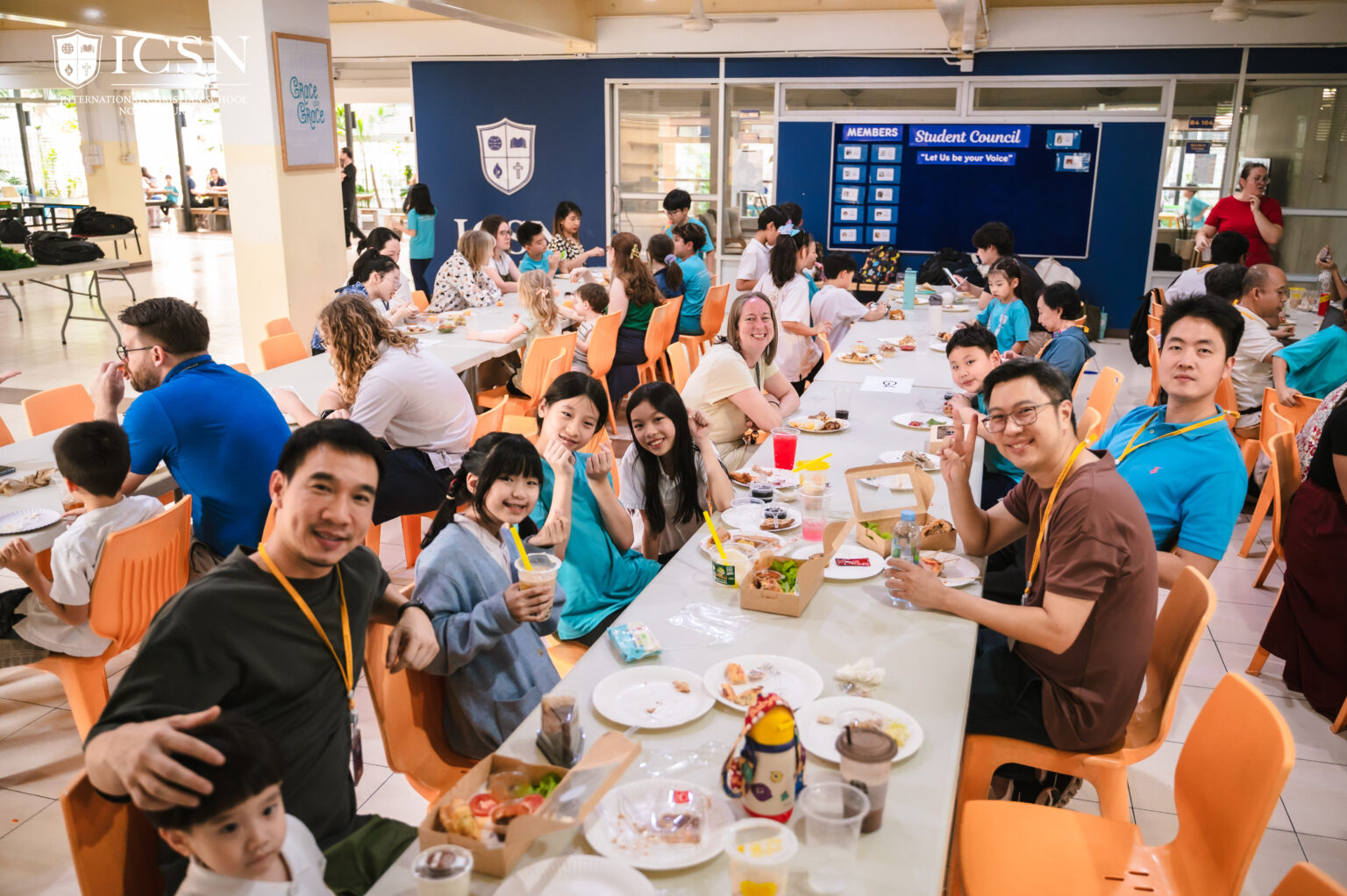 A long table with students, parents, and teachers at a parent-teacher’s potluck