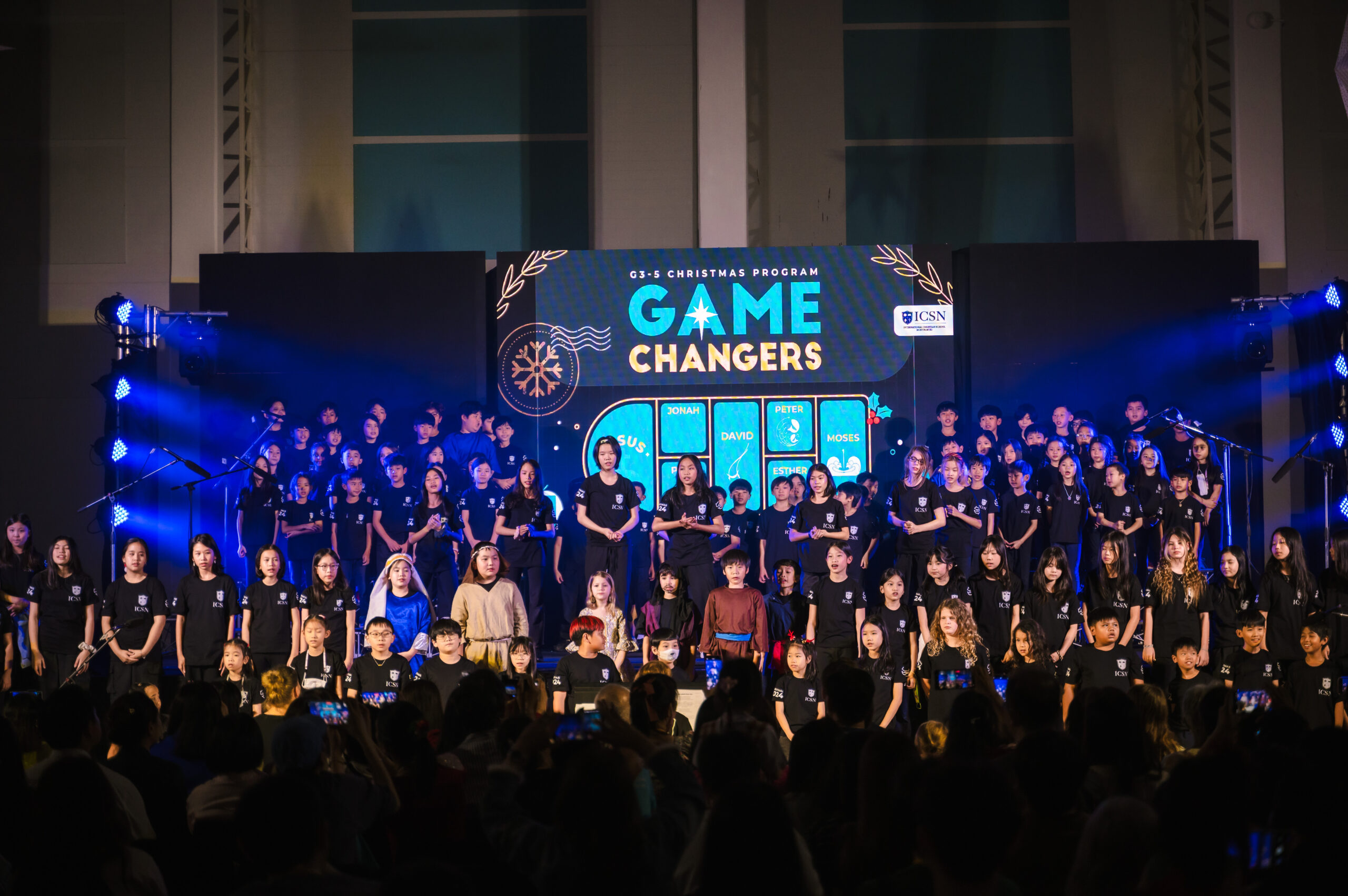 Students on stage performing a song with a back drop saying “Game Changers”