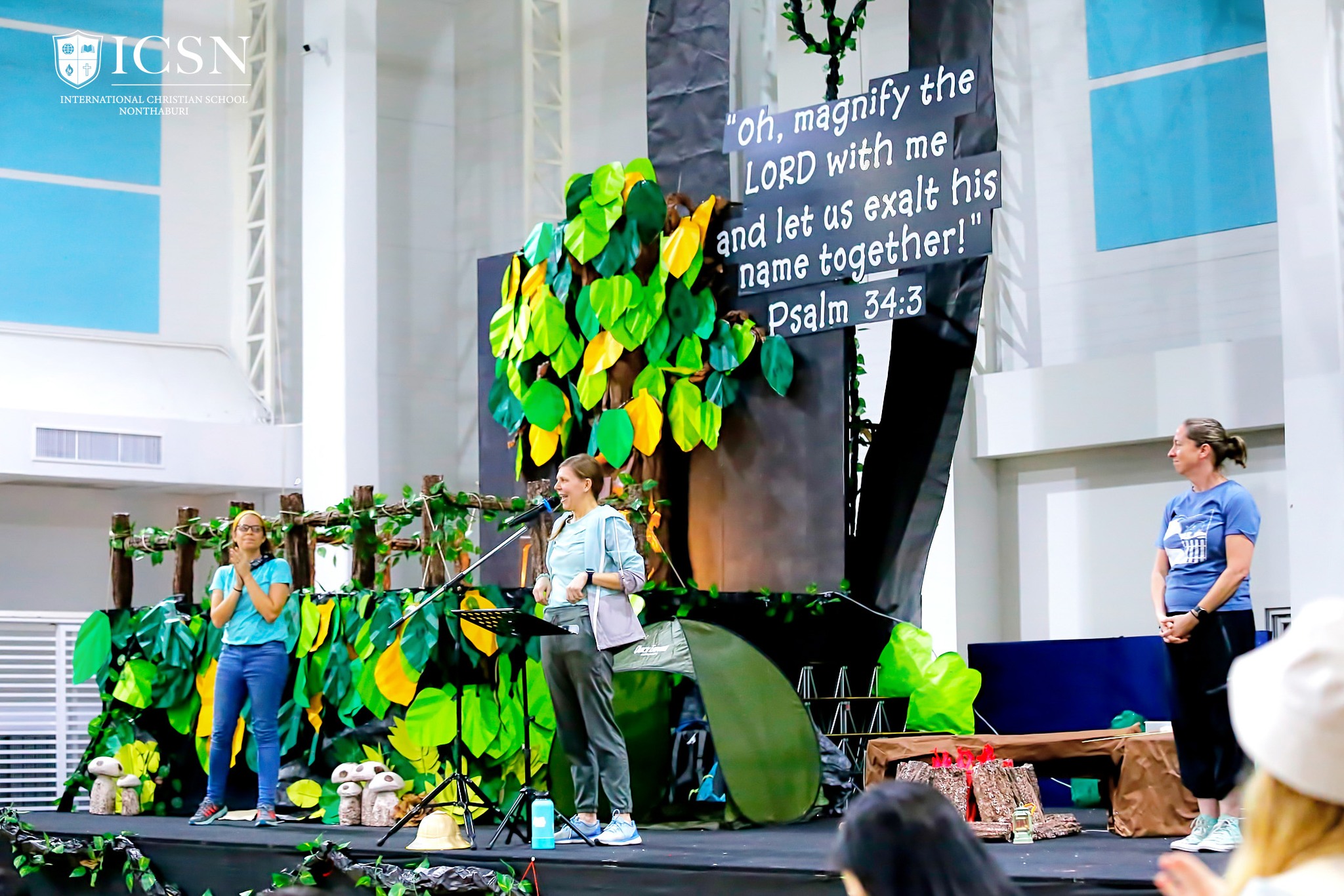 Three teachers on stage with a jungle-themed back drop and a Bible verse
