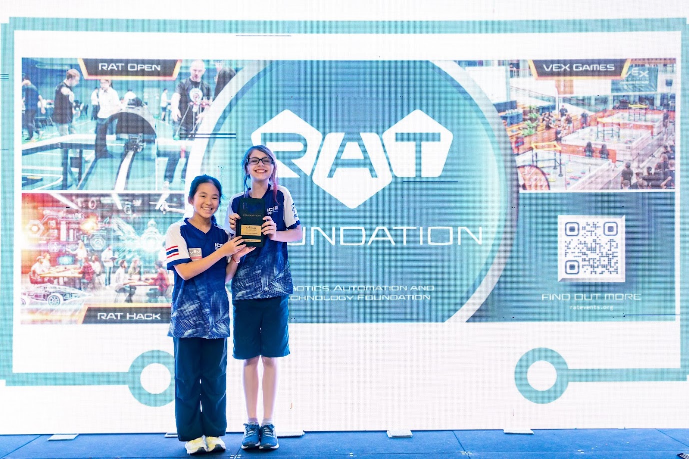 two girls receiving an award on stage with a blue-themed backdrop
