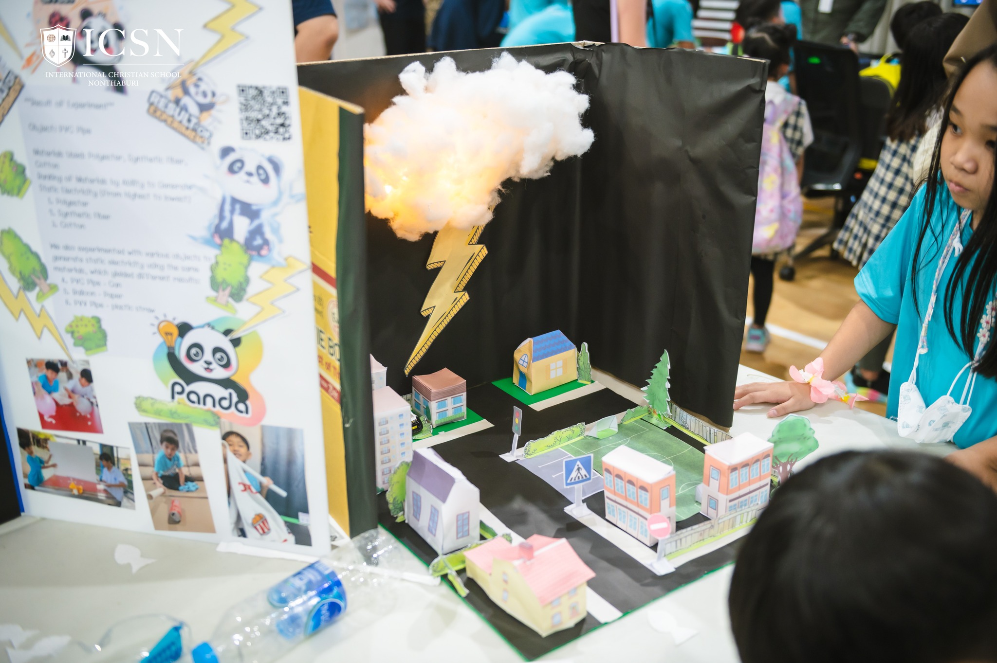A science fair project showcasing a village housing model with a cloud and lightning decor hovering over it