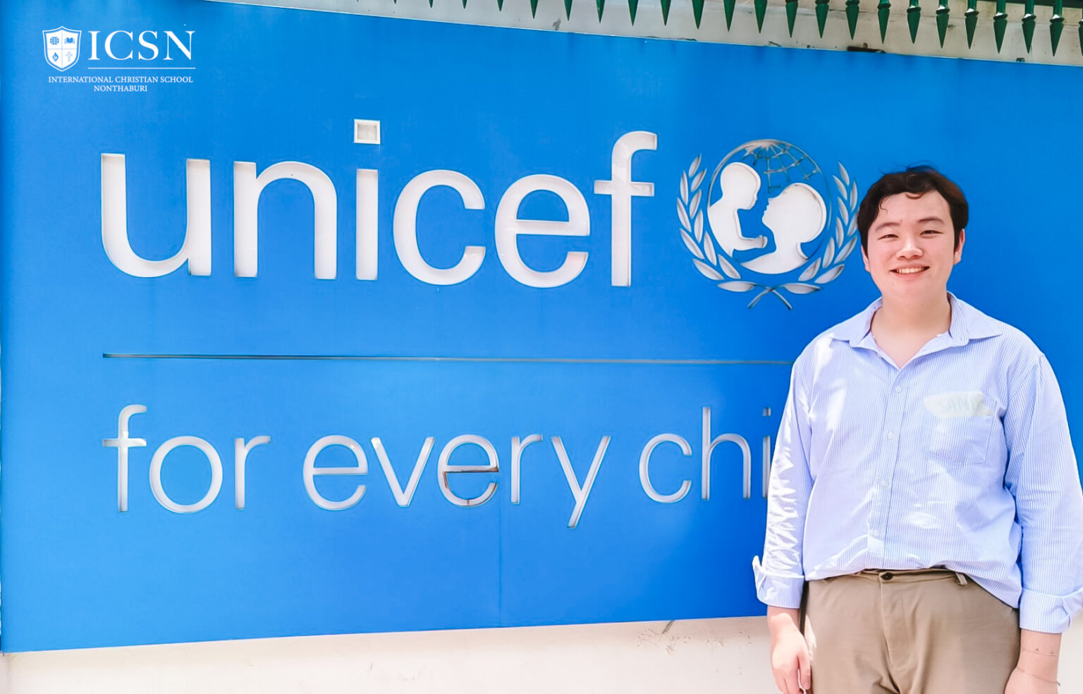 A student intern smiling in front of a Unicef sign during an international dialogue