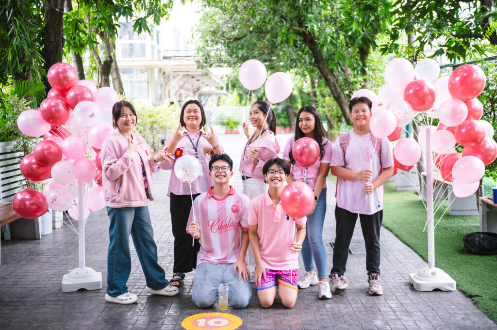 Students and teachers wearing pink, surrounded by red and pink balloons posing for a picture