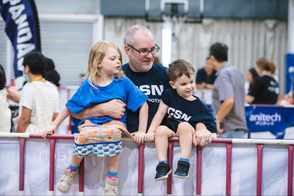 A family with a dad and two kids watching a robotics competition