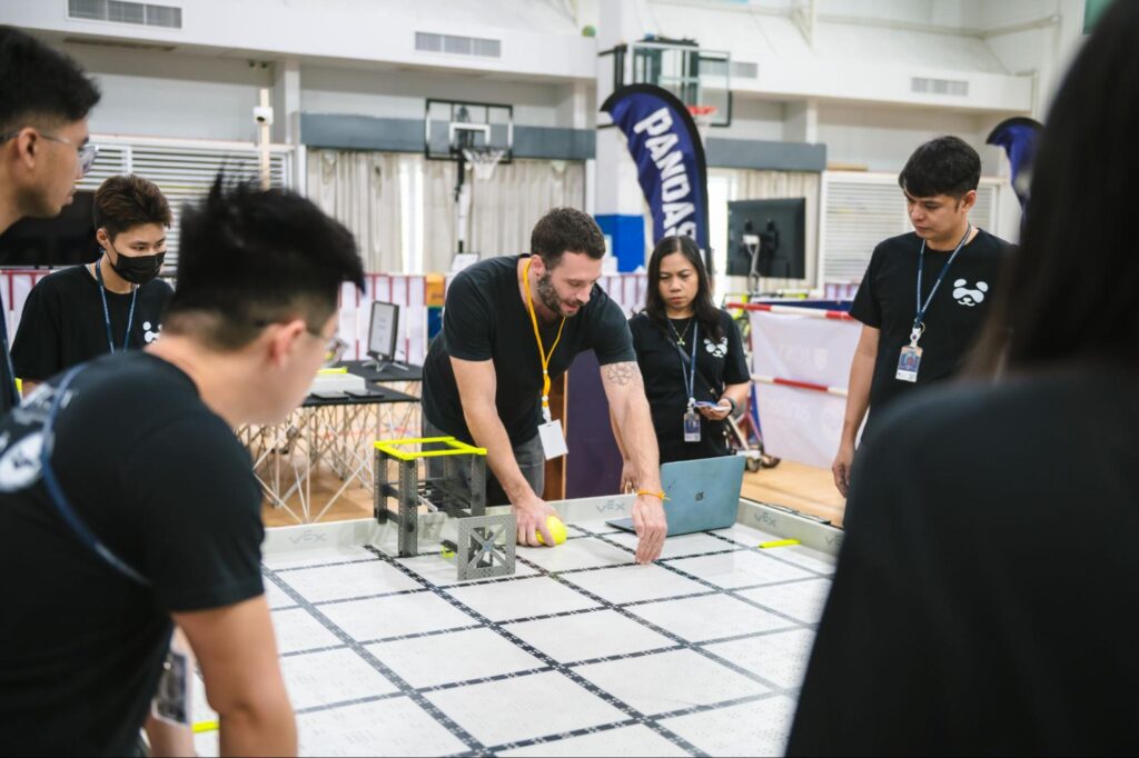 a team of people around a robotics field discussing a match