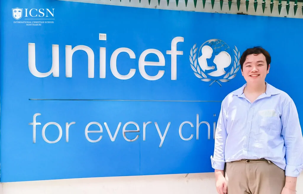 A student intern smiling in front of a Unicef sign during an international dialogue
